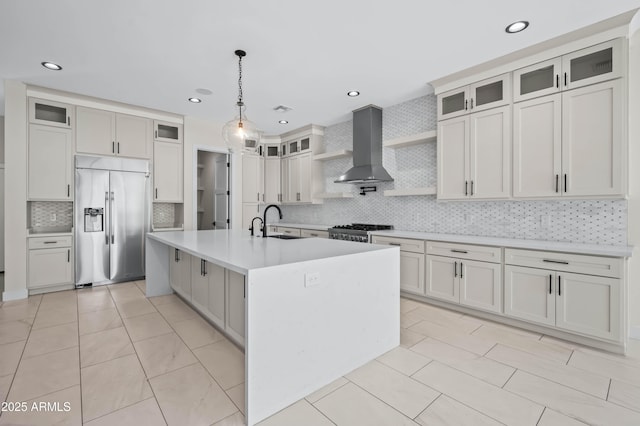 kitchen with built in refrigerator, a center island with sink, a sink, wall chimney range hood, and range