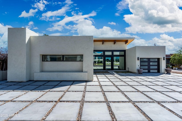 view of front facade with stucco siding, an attached garage, and a patio area