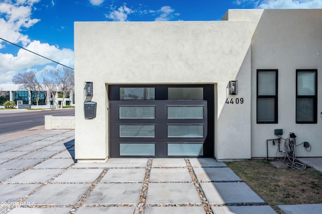 view of exterior entry featuring stucco siding, a garage, and concrete driveway