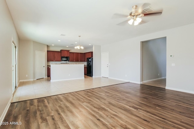 24479 W Mobile Ln, Buckeye, AZ 85326 - unfurnished living room with baseboards, light wood-style floors, and ceiling fan with notable chandelier