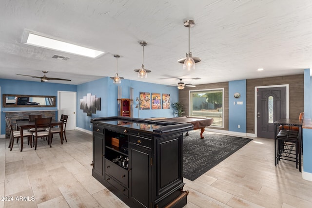 kitchen with pendant lighting, a kitchen breakfast bar, ceiling fan, light wood-type flooring, and a textured ceiling