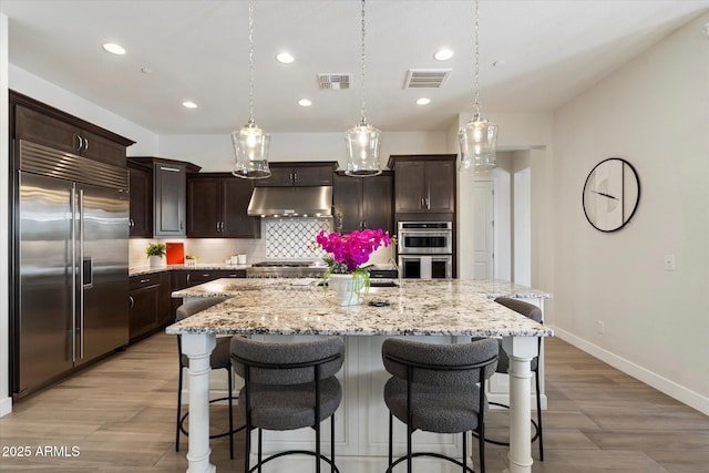 2821 E Cashman Dr, Phoenix, AZ 85050 - kitchen featuring stainless steel appliances, under cabinet range hood, baseboards, tasteful backsplash, and a breakfast bar area