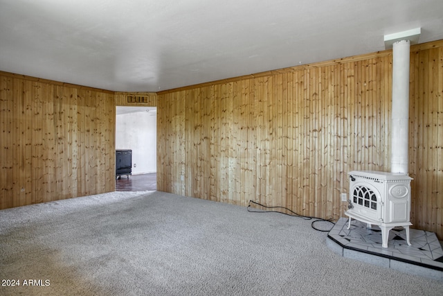 carpeted spare room with a wood stove and wood walls