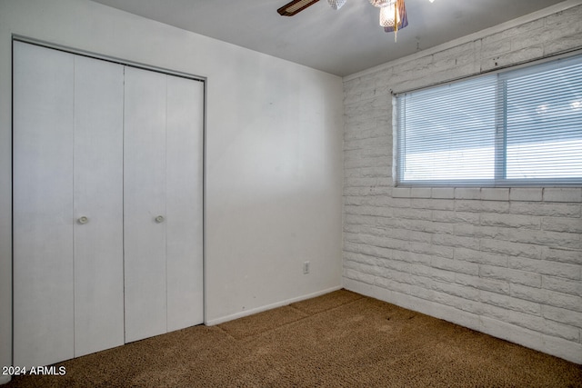 unfurnished bedroom with carpet flooring, ceiling fan, a closet, and brick wall