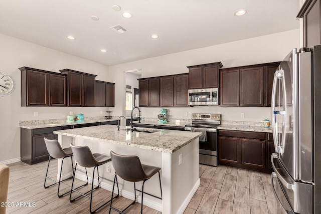 kitchen with sink, appliances with stainless steel finishes, a breakfast bar area, and an island with sink