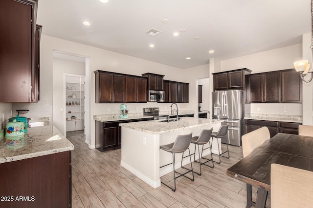 kitchen featuring light stone countertops, appliances with stainless steel finishes, sink, a center island with sink, and a breakfast bar area