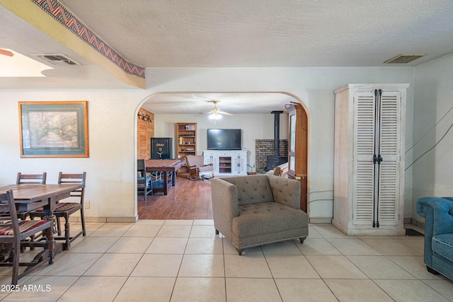 tiled living room featuring ceiling fan, a textured ceiling, and a wood stove