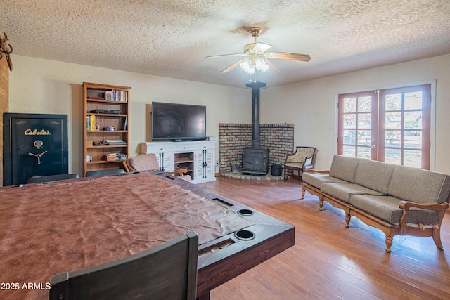 living room featuring hardwood / wood-style flooring, a wood stove, a textured ceiling, and ceiling fan