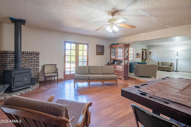 living room with a wood stove, light wood-type flooring, ceiling fan, a textured ceiling, and french doors