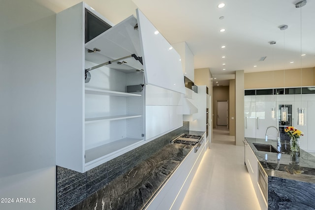 kitchen with pendant lighting, sink, built in shelves, dark stone countertops, and white cabinetry