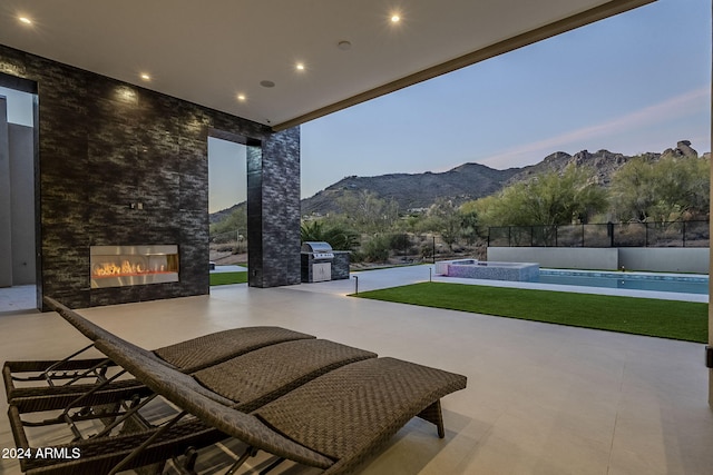 patio terrace at dusk featuring a mountain view, a fenced in pool, grilling area, and exterior kitchen