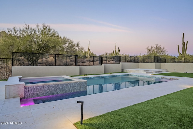 pool at dusk with an in ground hot tub and a lawn