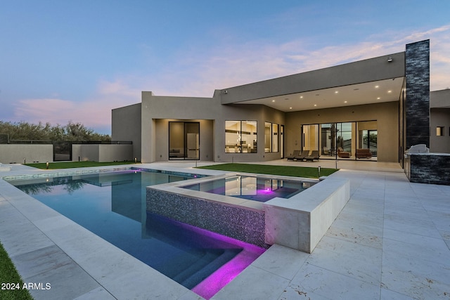 pool at dusk featuring an in ground hot tub and a patio