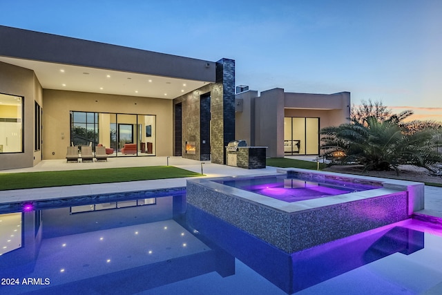 pool at dusk featuring an outdoor kitchen, an in ground hot tub, and a patio