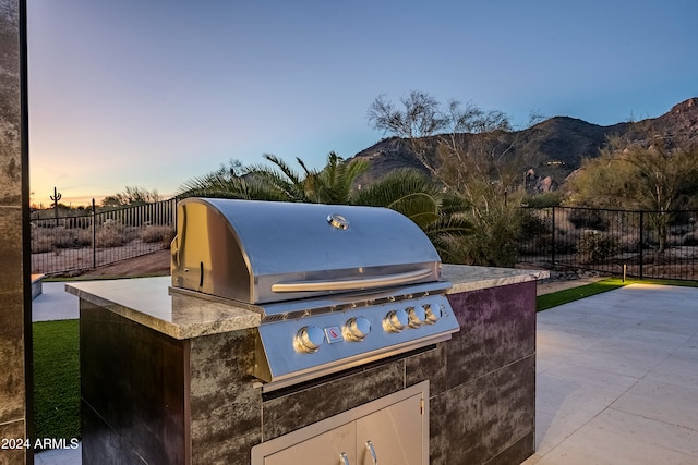 patio terrace at dusk with a mountain view, grilling area, and an outdoor kitchen