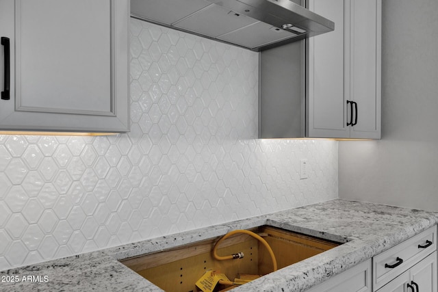 kitchen featuring wall chimney range hood, backsplash, and light stone countertops