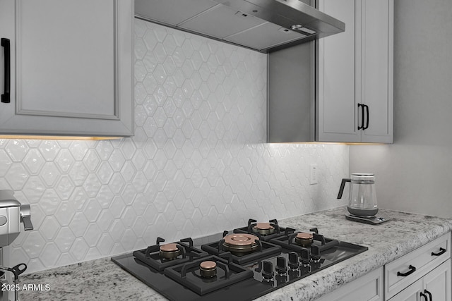 kitchen with black gas cooktop, white cabinetry, decorative backsplash, light stone countertops, and wall chimney exhaust hood