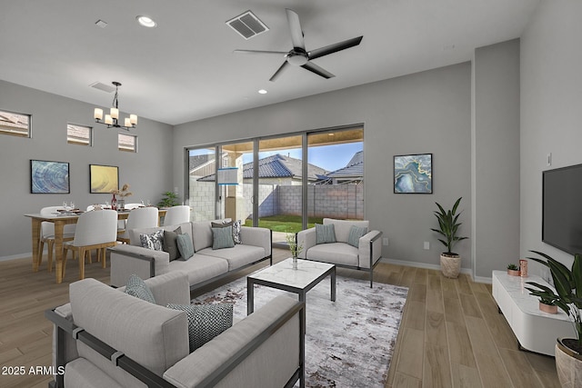 living room featuring ceiling fan with notable chandelier and light wood-type flooring