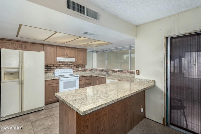 kitchen featuring light stone counters, sink, white appliances, and kitchen peninsula