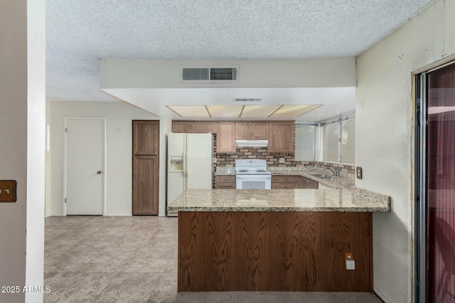 kitchen featuring kitchen peninsula, white appliances, a textured ceiling, light stone counters, and sink