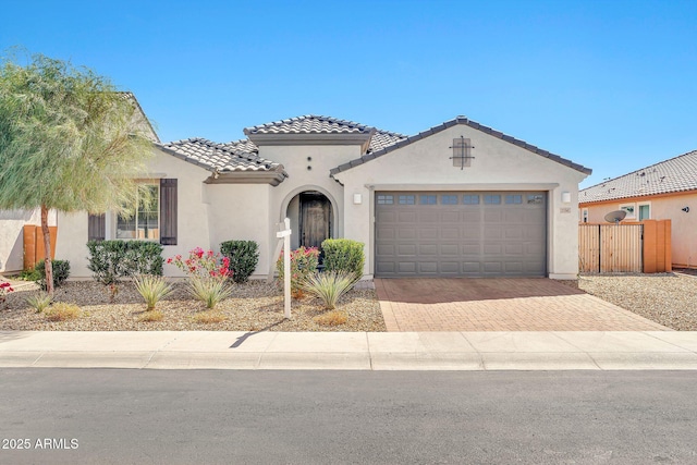 mediterranean / spanish-style home with an attached garage, fence, a tile roof, decorative driveway, and stucco siding