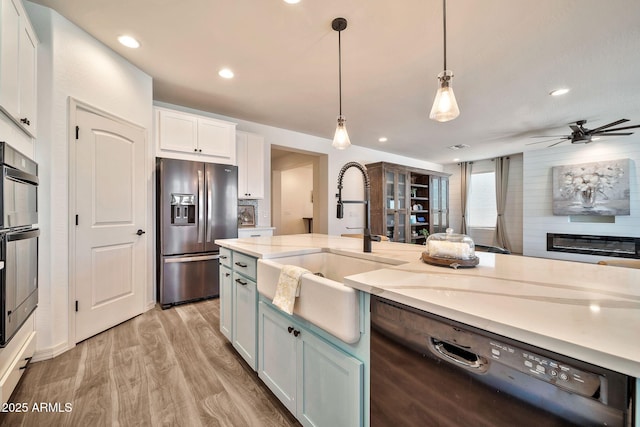 kitchen featuring stainless steel fridge, dishwasher, light wood-style flooring, white cabinetry, and a sink