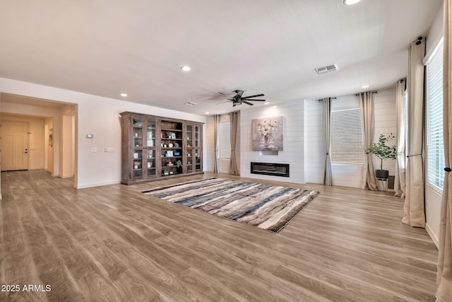 unfurnished living room with ceiling fan, recessed lighting, a large fireplace, visible vents, and light wood-style floors