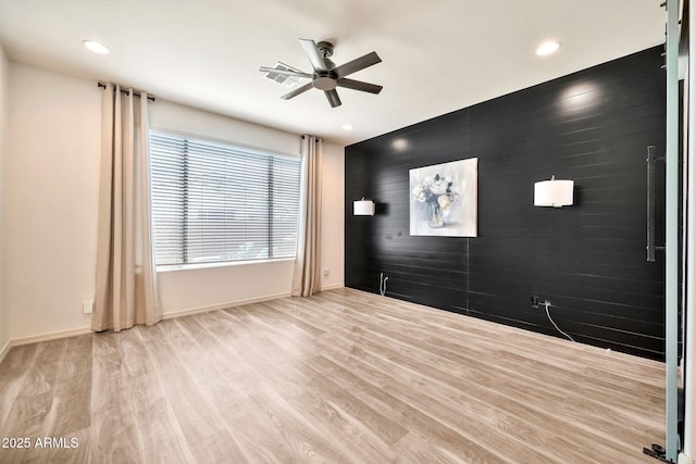 unfurnished room featuring an accent wall, a ceiling fan, wood walls, wood finished floors, and baseboards