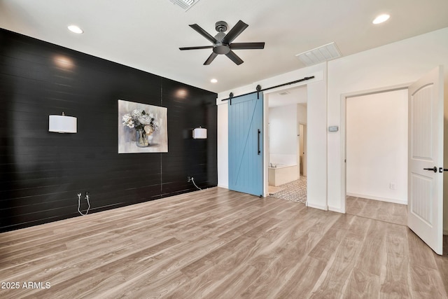 spare room featuring a barn door, visible vents, a ceiling fan, an accent wall, and wood finished floors