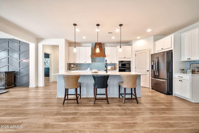 kitchen with white cabinets, stainless steel fridge with ice dispenser, light countertops, light wood-type flooring, and premium range hood