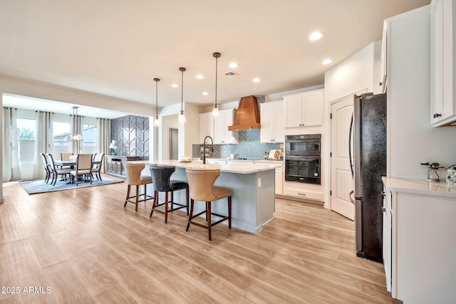 kitchen featuring custom range hood, a kitchen breakfast bar, light wood-type flooring, black appliances, and a sink