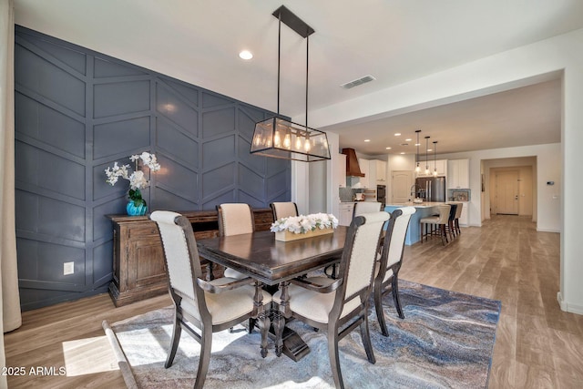 dining space with an accent wall, light wood-style floors, visible vents, and a decorative wall