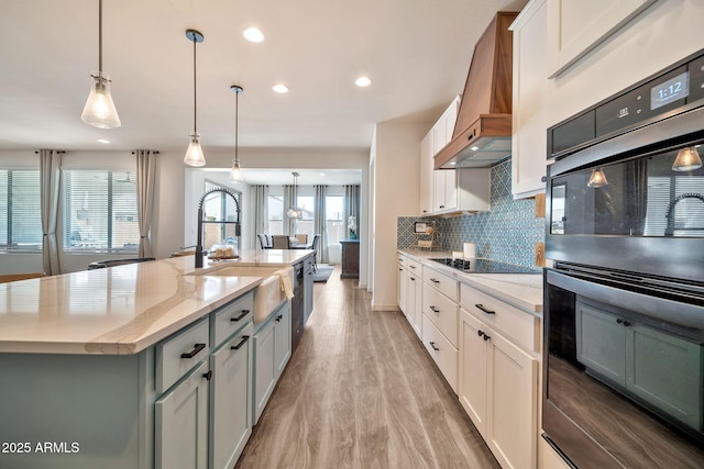 kitchen featuring a sink, custom exhaust hood, decorative backsplash, black appliances, and light wood finished floors