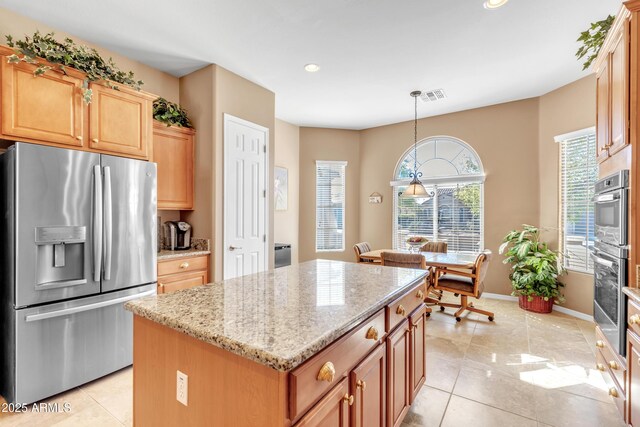 kitchen with light stone countertops, visible vents, a kitchen island, light tile patterned flooring, and stainless steel appliances