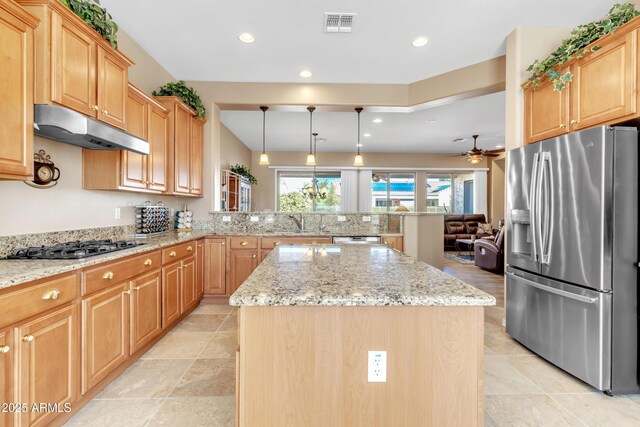 kitchen with under cabinet range hood, light stone countertops, appliances with stainless steel finishes, and a center island