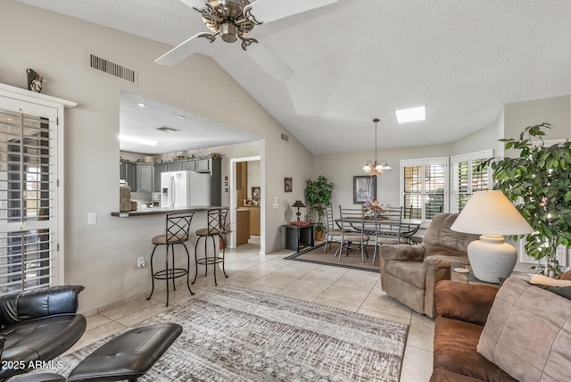 living room featuring light tile patterned floors, vaulted ceiling, ceiling fan with notable chandelier, and visible vents