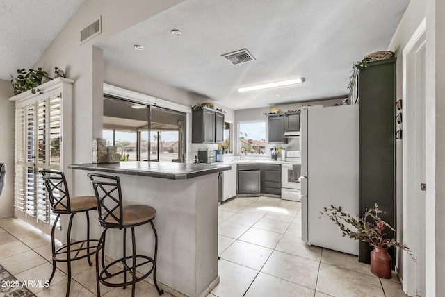 kitchen featuring a peninsula, white appliances, light tile patterned floors, and visible vents