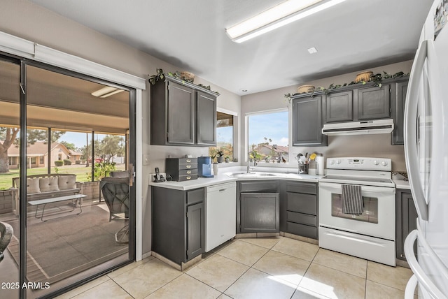 kitchen with light tile patterned floors, under cabinet range hood, white appliances, a sink, and light countertops