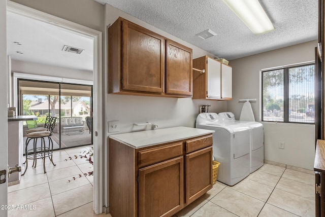 clothes washing area with visible vents, cabinet space, washing machine and dryer, light tile patterned flooring, and a textured ceiling