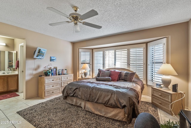 bedroom featuring light tile patterned floors, a textured ceiling, a sink, a ceiling fan, and ensuite bath