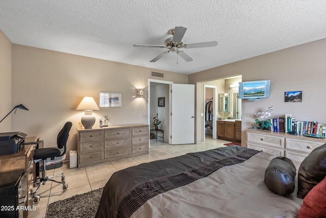 bedroom featuring a textured ceiling, ensuite bathroom, light tile patterned flooring, a ceiling fan, and visible vents