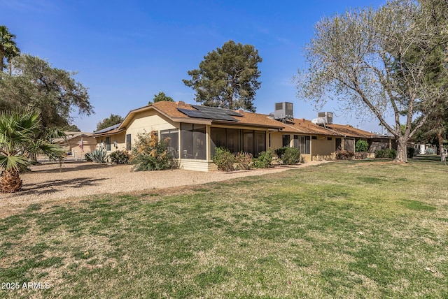 rear view of property featuring a sunroom, a lawn, and solar panels