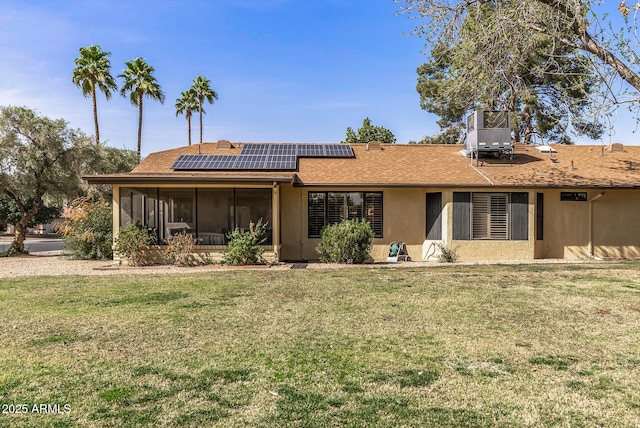 back of house with a shingled roof, solar panels, a lawn, a sunroom, and stucco siding