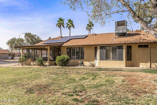 view of front facade with central air condition unit, stucco siding, a front yard, a sunroom, and roof mounted solar panels