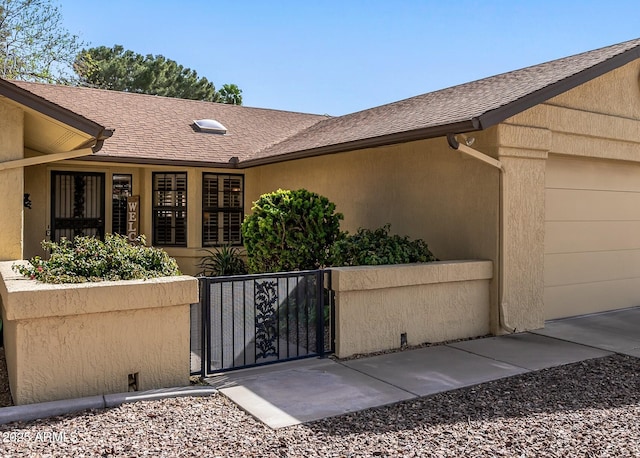 doorway to property featuring a garage, a shingled roof, fence, a gate, and stucco siding