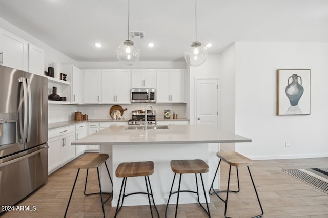 kitchen featuring white cabinets, stainless steel appliances, a kitchen island with sink, and sink