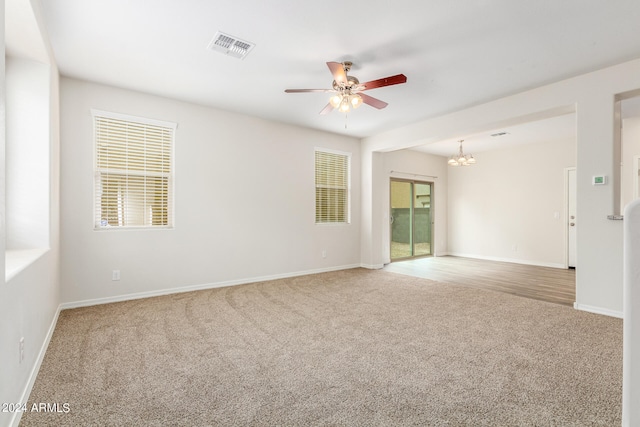 carpeted spare room featuring ceiling fan with notable chandelier