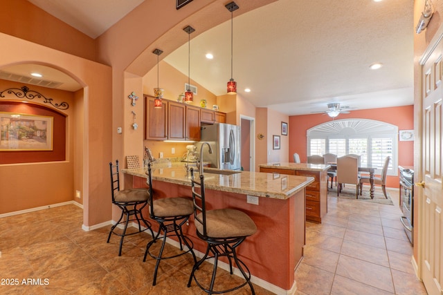 kitchen with light stone counters, stainless steel appliances, brown cabinetry, a peninsula, and a kitchen bar