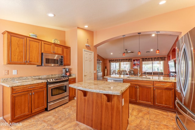 kitchen with light stone counters, brown cabinets, a center island, stainless steel appliances, and a sink