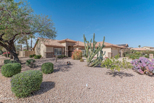 mediterranean / spanish-style home with a tile roof, stucco siding, an attached garage, fence, and stone siding